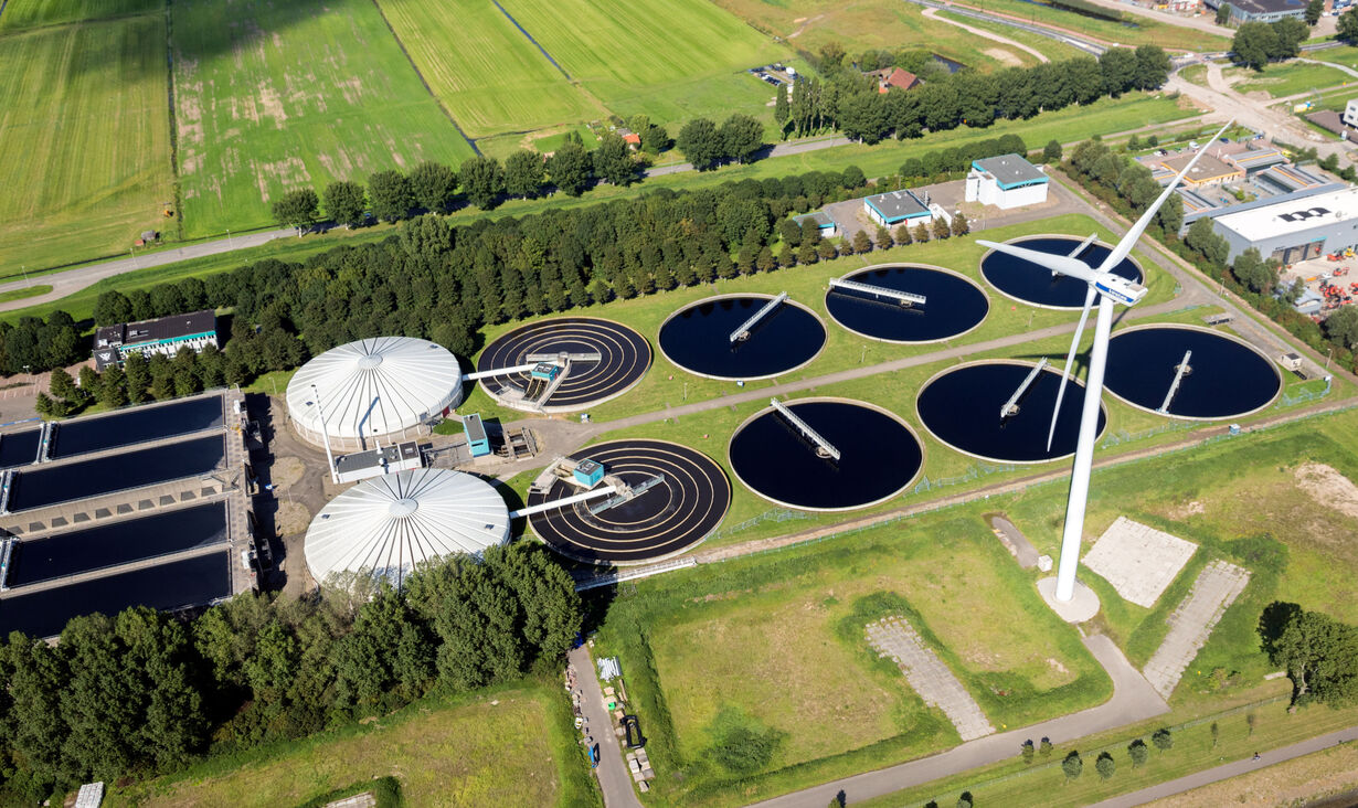 Luftaufnahme einer Kläranlage mit Windkraftanlage und runden Becken.