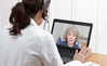 Healthcare professional in a video call with an elderly woman on a laptop screen.